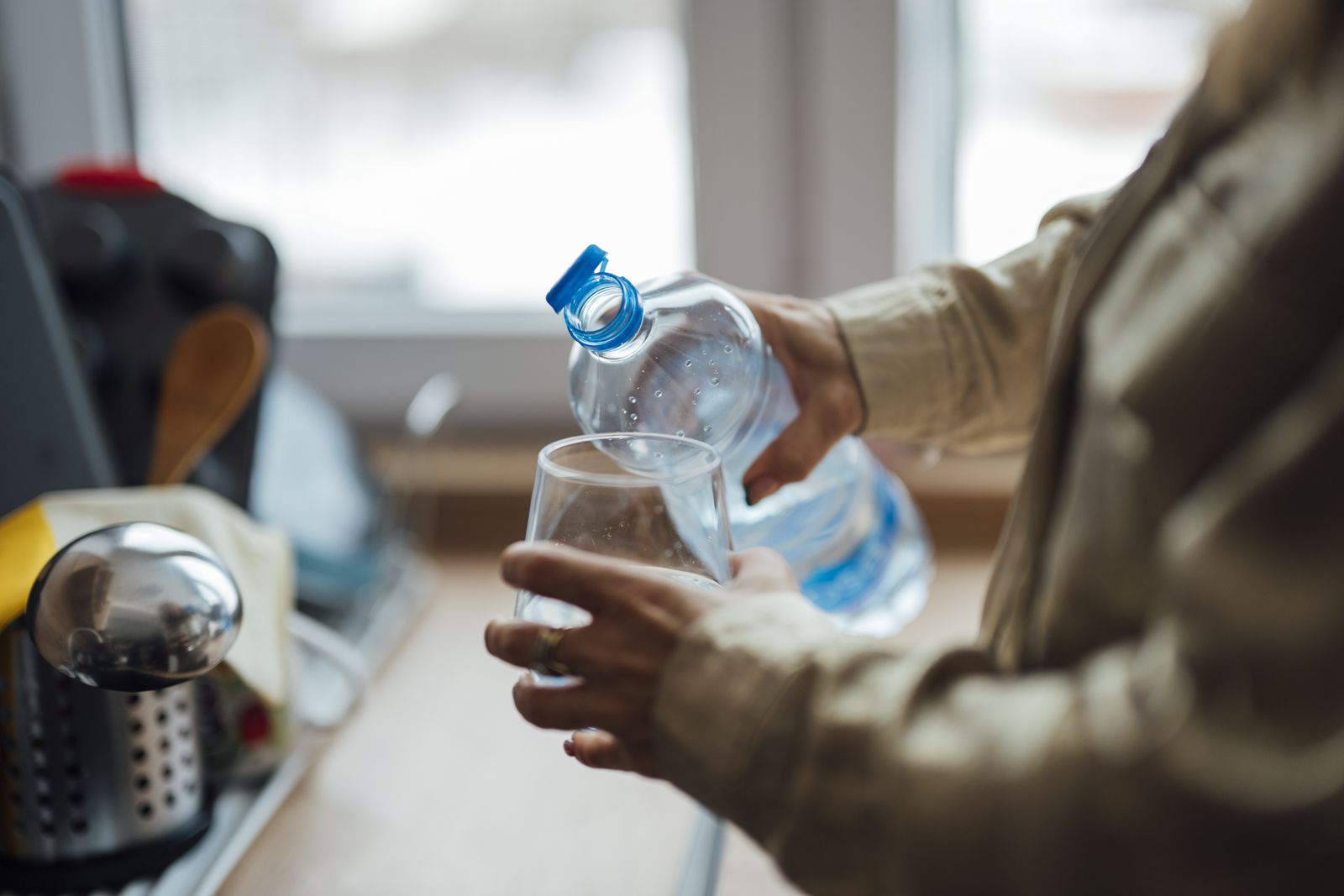 A person pouring water from a bottle into a glass in a kitchen